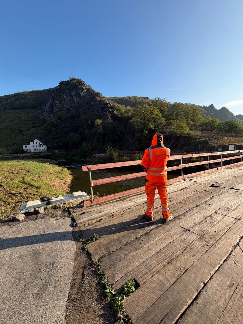 Mitarbeiter in oranger Warnkleidung mit CG-Bau-Logo auf einer Behelfsbrücke über einem Fluss
