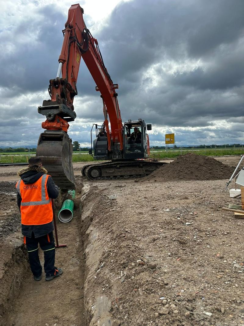 Mitarbeiter mit Warnweste im Graben vor dem Bagger