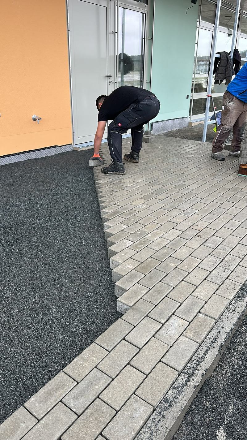 Mitarbeiter setzt Pflastersteine an der Kante zu einem dunklen Fallschutzbelag