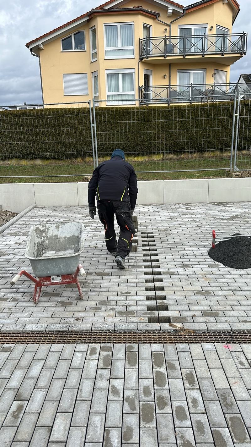 Mitarbeiter verlegt Pflaster an einer Entwässerungsrinne vor einem Wohnhaus